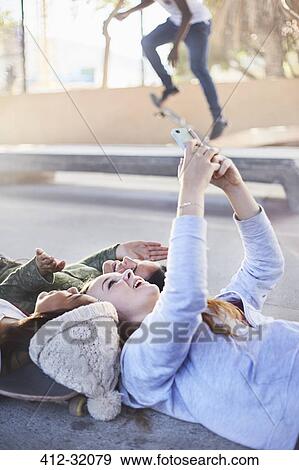 Stock Photo - Teenage girls laying taking selfie with camera phone at skate park. Fotosearch