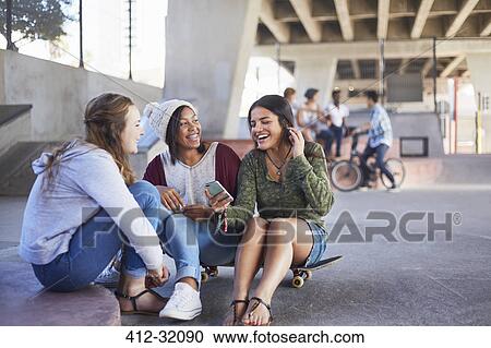 Stock Image - Teenage girls on skateboard texting and hanging out at skate park. Fotosearch