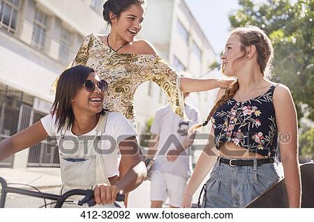 Stock Image - Teenage girls with BMX bicycle and skateboard on sunny urban street. Fotosearch