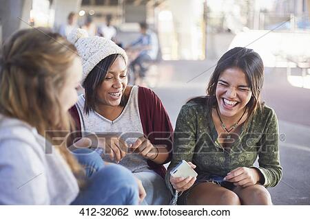 Stock Image - Teenage girls with cell phone laughing and hanging out. Fotosearch
