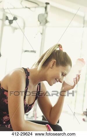 Picture - Tired woman cooling forehead with water bottle at gym. Fotosearch