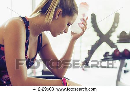 Tired woman cooling forehead with water bottle at gym View Large Photo Image Stock Image - Tired woman cooling forehead with water bottle at gym. Fotosearch