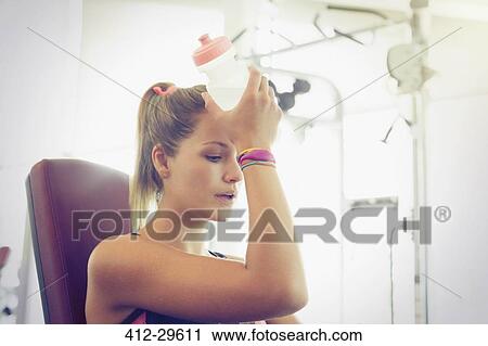 Tired woman cooling forehead with water bottle at gym View Large Photo Image Stock Image - Tired woman cooling forehead with water bottle at gym. Fotosearch