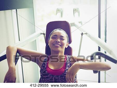 Stock Photography - Tired woman resting at exercise equipment in gym. Fotosearch