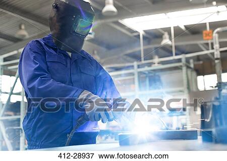 Stock Photo - Welder in protective workwear using welding torch in steel factory. Fotosearch