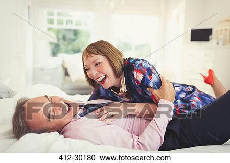 Stock Image - Well-dressed mature couple laughing on bed. Fotosearch