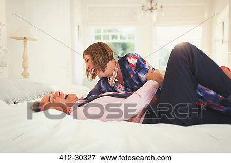 Stock Photo - Well-dressed mature couple laughing on bed. Fotosearch