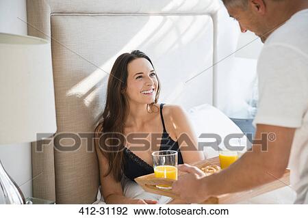 Wife smiling at husband serving breakfast in bed View Large Photo Image Stock Image - Wife smiling at husband serving breakfast in bed. Fotosearch