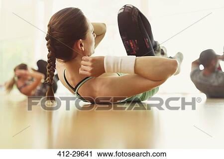 Stock Image - Woman doing bicycle sit-ups in exercise class. Fotosearch