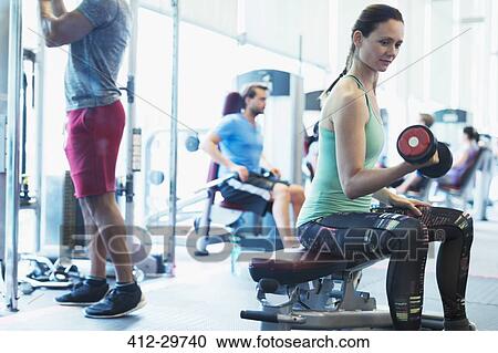 Stock Image - Woman doing dumbbell biceps curls at gym. Fotosearch