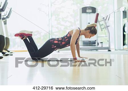 Stock Photograph - Woman doing push-ups on knees at gym. Fotosearch