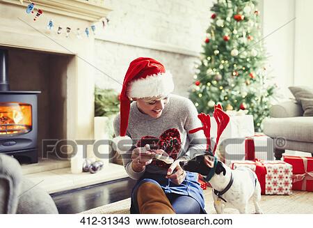 Stock Image - Woman giving bone to dog wearing Christmas reindeer antlers. Fotosearch