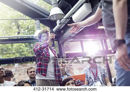 Picture - Woman in audience handing speaker microphone at conference. Fotosearch