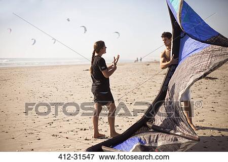 Stock Photo - Woman instructing man with kiteboarding kite on sunny beach. Fotosearch