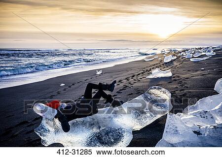 Woman laying on large ice chunk on beach at sunset, Iceland View Large Photo Image Stock Photography - Woman laying on large ice chunk on beach at sunset, Iceland. Fotosearch