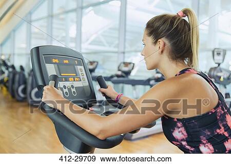 Stock Photo - Woman riding exercise bike at gym. Fotosearch