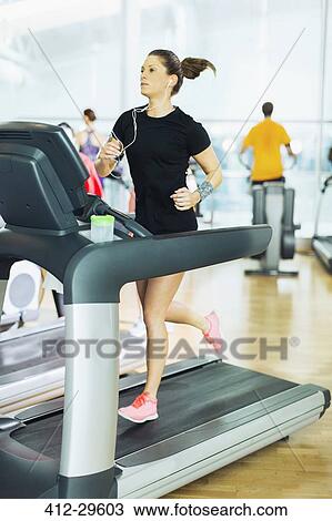 Woman running on treadmill with headphones at gym View Large Photo Image Stock Image - Woman running on treadmill with headphones at gym. Fotosearch