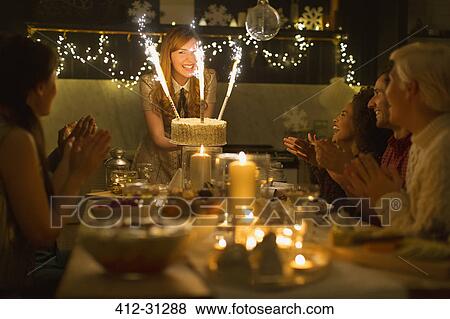 Stock Photo - Woman serving Christmas cake with sparkler fireworks to clapping family. Fotosearch