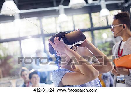 Picture - Woman trying virtual reality stimulator glasses at technology conference. Fotosearch
