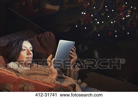 Woman using digital tablet relaxing on sofa in living room near Christmas tree View Large Photo Image Stock Image - Woman using digital tablet relaxing on sofa in living room near Christmas tree. Fotosearch