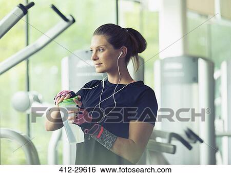 Stock Photograph - Woman with headphones resting and drinking water at gym. Fotosearch