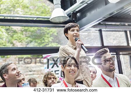 Stock Image - Woman with microphone asking question in audience at conference. Fotosearch