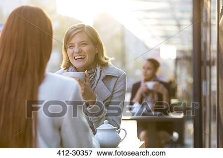 Stock Photo - Women laughing and drinking tea at sidewalk cafe. Fotosearch