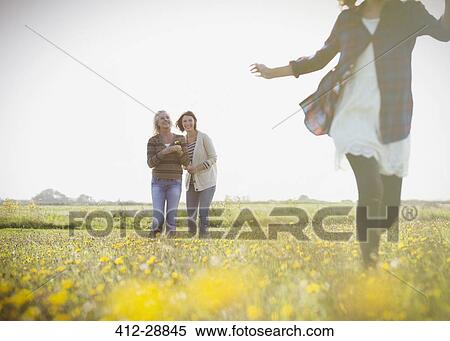 Stock Photography - Women watching girl run in sunny meadow with wildflowers. Fotosearch