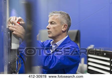 Stock Photo - Worker adjusting machinery in steel factory. Fotosearch