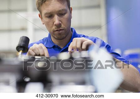 Stock Image - Worker examining machinery in steel factory. Fotosearch
