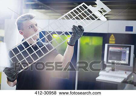 Stock Photo - Worker examining piece in steel factory. Fotosearch