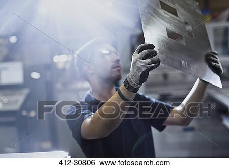Stock Photograph - Worker examining piece in steel factory. Fotosearch
