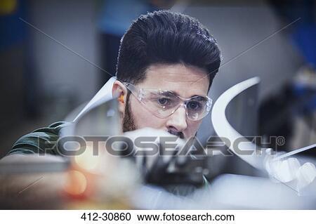 Stock Image - Worker examining pieces in steel factory. Fotosearch
