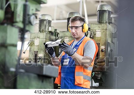 Stock Image - Worker in protective workwear examining part in factory. Fotosearch