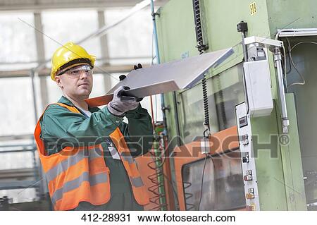 Worker in protective workwear examining steel part in factory View Large Photo Image Stock Image - Worker in protective workwear examining steel part in factory. Fotosearch