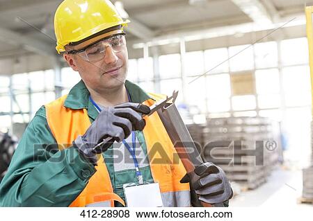 Worker in protective workwear examining part in factory View Large Photo Image Stock Photo - Worker in protective workwear examining part in factory. Fotosearch