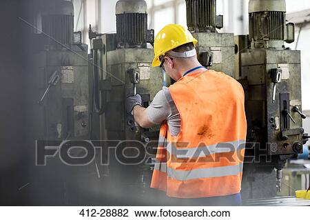 Stock Image - Worker in protective workwear operating machinery in factory. Fotosearch