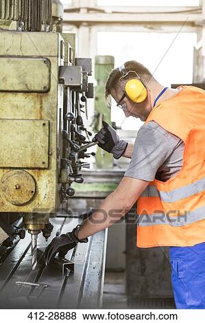 Stock Photo - Worker in protective workwear operating machinery in factory. Fotosearch