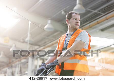 Worker in protective workwear pulling pallet truck in factory View Large Photo Image Stock Photo - Worker in protective workwear pulling pallet truck in factory. Fotosearch