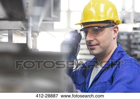 Stock Photo - Worker in protective workwear using flashlight in factory. Fotosearch