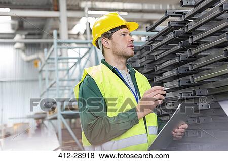 Worker in protective workwear with clipboard examining steel parts in factory View Large Photo Image Stock Photo - Worker in protective workwear with clipboard examining steel parts in factory. Fotosearch