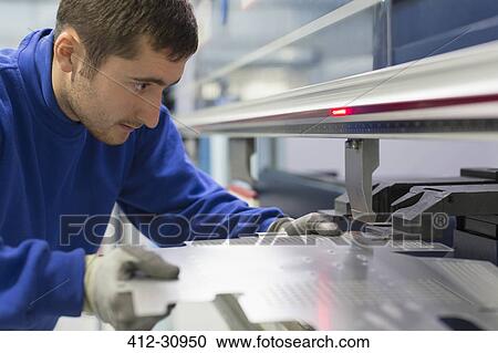 Stock Image - Worker operating laser cutter in steel factory. Fotosearch