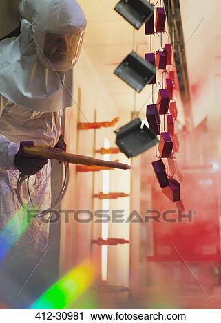 Stock Image - Worker painting steel pieces red in steel factory. Fotosearch