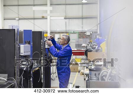 Stock Image - Worker repairing machinery in steel factory. Fotosearch