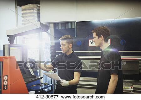 Stock Photo - Worker training trainee at machinery control panel in steel factory. Fotosearch