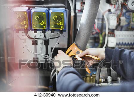 Stock Image - Worker using tool on machinery in steel factory. Fotosearch