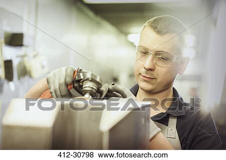 Stock Photo - Worker using tool on part in steel factory. Fotosearch