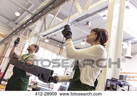 Stock Photo - Workers hanging steel part in factory. Fotosearch