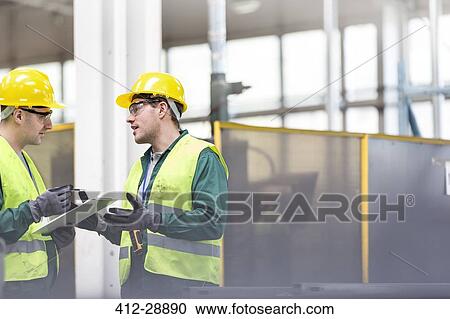 Stock Image - Workers in protective workwear talking with clipboard. Fotosearch