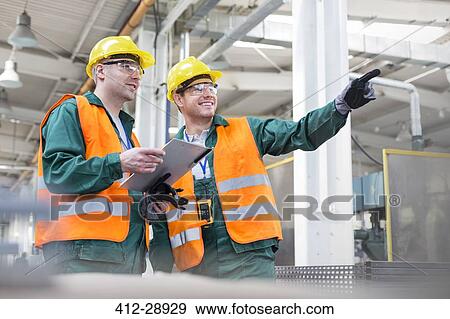Workers in protective workwear talking with clipboard in factory View Large Photo Image Stock Photo - Workers in protective workwear talking with clipboard in factory. Fotosearch